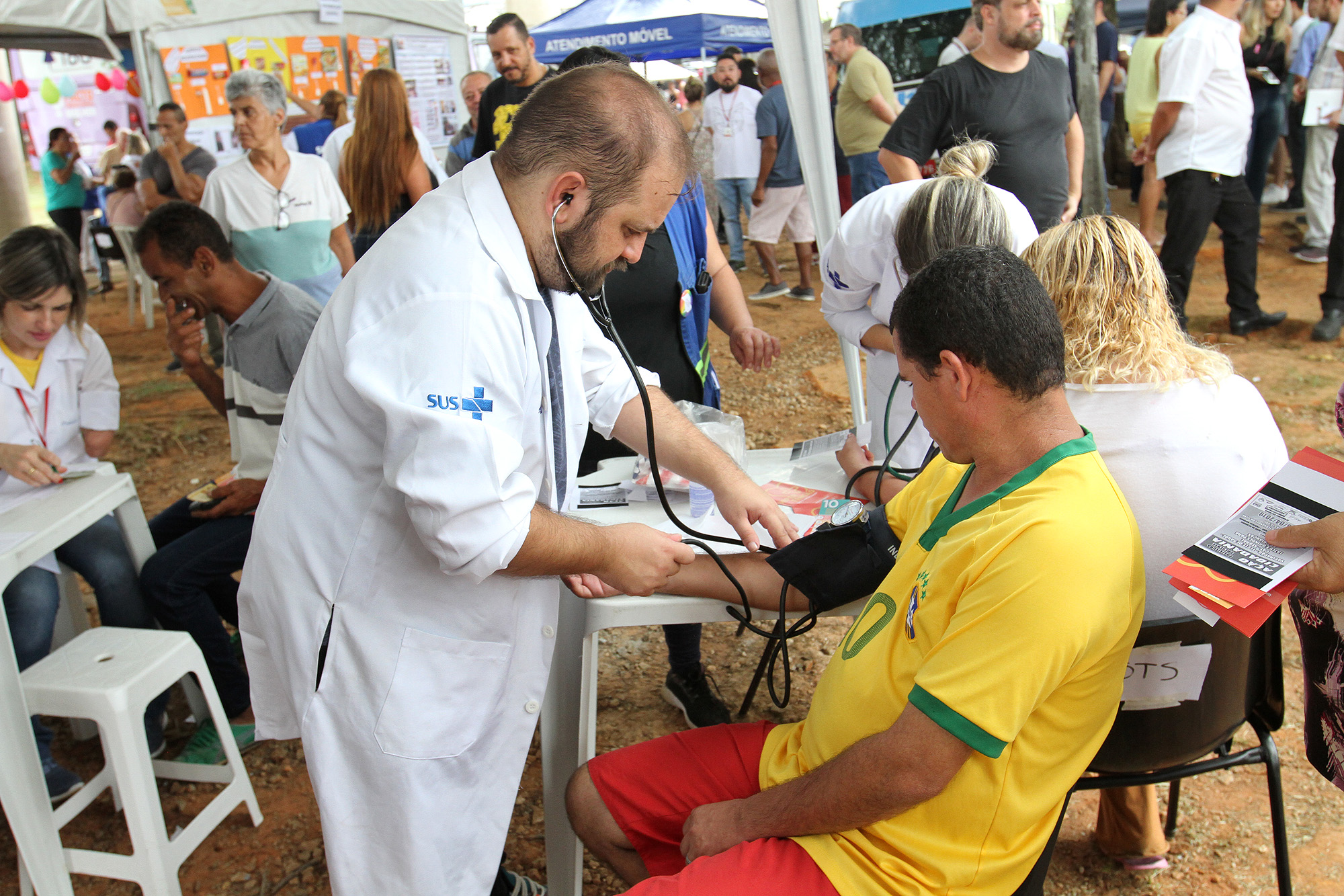 Foto de médico aferindo pressão arterial de munícipe, que está sentado, durante Mutirão nos Bairros na Praça Felisberto Fernandes da Silva, em São Mateus